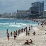 People walk down the beach in Cancún with high-rise hotels in the background