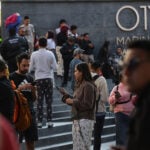 A crowd of people in pijamas stands outside a Mexico City building, many checking their cellphones