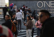 A crowd of people in pijamas stands outside a Mexico City building, many checking their cellphones