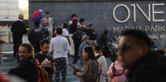 A crowd of people in pijamas stands outside a Mexico City building, many checking their cellphones