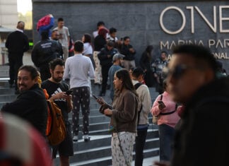 A crowd of people in pijamas stands outside a Mexico City building, many checking their cellphones