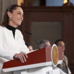 President Sheinbaum smiles behind a press conference podium