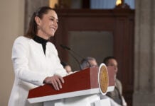 President Sheinbaum smiles behind a press conference podium