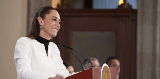 President Sheinbaum smiles behind a press conference podium