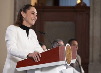 President Sheinbaum smiles behind a press conference podium