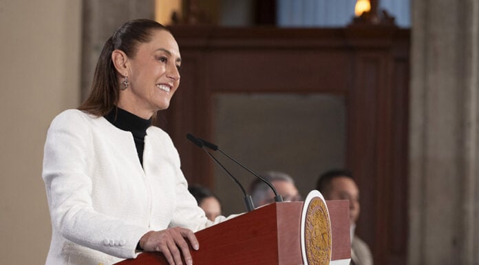 President Sheinbaum smiles behind a press conference podium