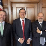 Marcelo Ebrard, Jamieson Greer and Howard Lutnick stand next to an American flag
