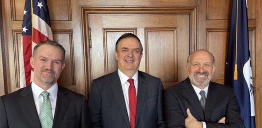 Marcelo Ebrard, Jamieson Greer and Howard Lutnick stand next to an American flag