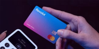 A hand holds a Revolut credit card next to a payment terminal