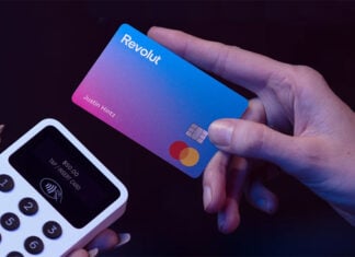 A hand holds a Revolut credit card next to a payment terminal