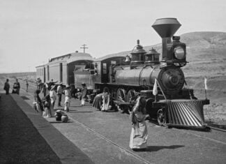 A vintage black-and-white photograph from the Porfiriato era, featuring Mexican campesinos in white and with straw hats and an elderly woman carrying a large ceramic cistern in front of a Ferrocarril Central Mexicano steam locomotive at a rural station in Mexico during the nation's Porfiriato era, which followed Porfirio Díaz's rise to power under the Plan of Tuxtepec.