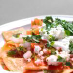 A close-up shot of a plate of red chilaquiles, a staple authentic Mexican recipe, topped with fresh crema, crumbled queso fresco, diced onions and cilantro.