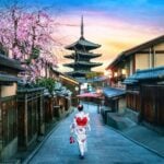 Beautiful sunset view of a Japanese street featuring cherry blossoms, traditional wooden buildings, and a pagoda in the background.