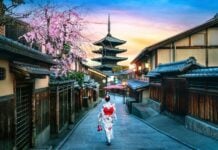 Beautiful sunset view of a Japanese street featuring cherry blossoms, traditional wooden buildings, and a pagoda in the background.