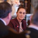 President Sheinbaum in focus, talking to a couple of men in business suits