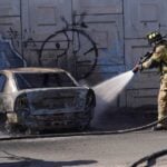 A firefighter extinguishes a burning car after violence following the death of El Mencho