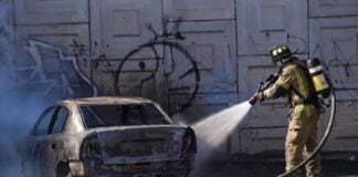 A firefighter extinguishes a burning car after violence following the death of El Mencho