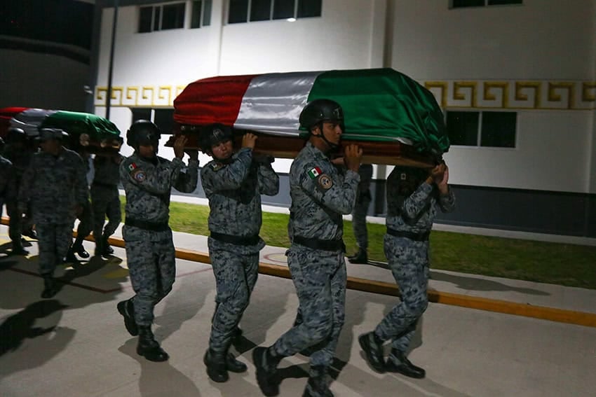 National Guard members in uniform carry caskets wrapped in the Mexican flag