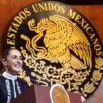 President Sheinbaum in front of a large seal reading Estados Unidos Mexicanos