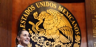 President Sheinbaum in front of a large seal reading Estados Unidos Mexicanos