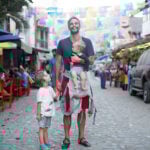 A man holds a baby and a child's hand standing on the street of a Mexican town