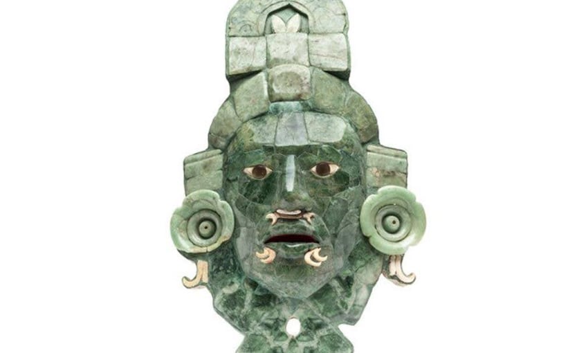 A mask made of jade found at the Calakmul archeological site. It has stones representing its eyes and carved circular embellishments near the figure on the mask's ears.