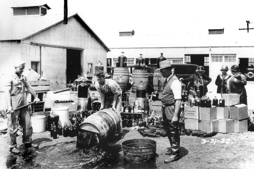 Black and white photo of men dumping barrels of illegal alcohol into public outdoor drains in California in 1932.