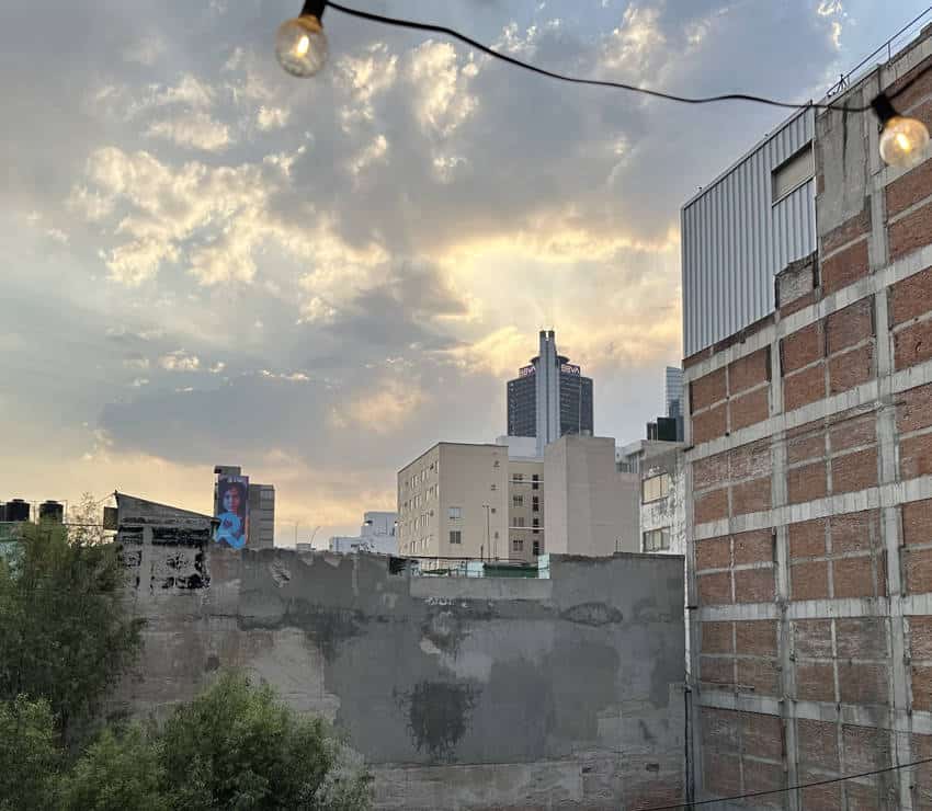 A rooftop view of Mexico City buildings and a cloudy sunset sky, showcasing the urban landscape