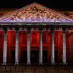 The neoclassical facade of the Teatro Degollado in Guadalajara, Mexico, illuminated at night with red and white lighting, showcasing its Corinthian columns and marble pediment relief of Apollo and the Nine Muses.