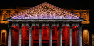 The neoclassical facade of the Teatro Degollado in Guadalajara, Mexico, illuminated at night with red and white lighting, showcasing its Corinthian columns and marble pediment relief of Apollo and the Nine Muses.