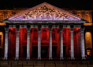 The neoclassical facade of the Teatro Degollado in Guadalajara, Mexico, illuminated at night with red and white lighting, showcasing its Corinthian columns and marble pediment relief of Apollo and the Nine Muses.