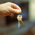 Image of a hand holding a set of golden keys on a keychain. The background image is bokeh.