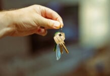 Image of a hand holding a set of golden keys on a keychain. The background image is bokeh.