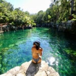 A woman sits at the edge of a Tulum cenote