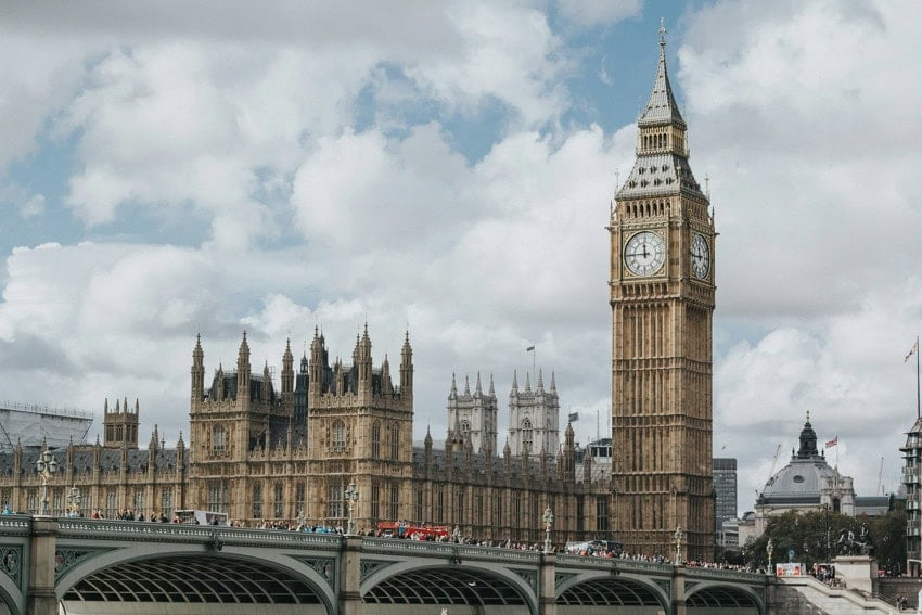 Photo of Big Ben and London Bridge and part of the city skyline against a partly cloudy blue sky.