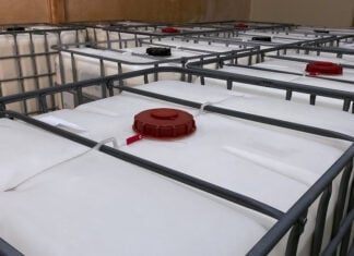 Low light view. Many large white tanks chemical packaging inside of the factory.