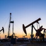 Oil pumps and a drilling rig at sunset