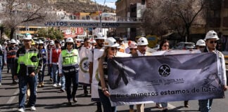 "Los mineros están en luto," reads a banner carried by a group protesting miners marching down a road
