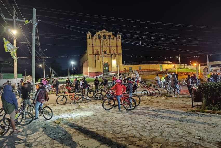 Bikers in street clothes and helmets gathered in a cobblestoned municipal plaza in San Cristobal de las Casas, Chiapas, Mexico. Some of them are chatting.