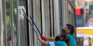 Un par de mujeres trabajan limpiando los cristales de un edificio en Paseo de la Reforma.