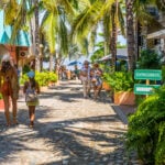 Tourists stroll beneath palm trees on the streets of Sayulita, Mexico