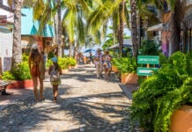 Tourists stroll beneath palm trees on the streets of Sayulita, Mexico
