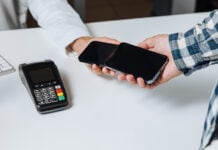 Two cell phones tap to trade a payment, with a card terminal visible in the corner