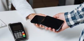 Two cell phones tap to trade a payment, with a card terminal visible in the corner