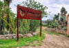 Nature trail in a semi-desert park with a wooden entrance sign that says in Spanish El Charco del Ingenio, jardin botanica. The entrance to the trail is winding and ringed on both sides by stone walls with landscaped cacti of various types.