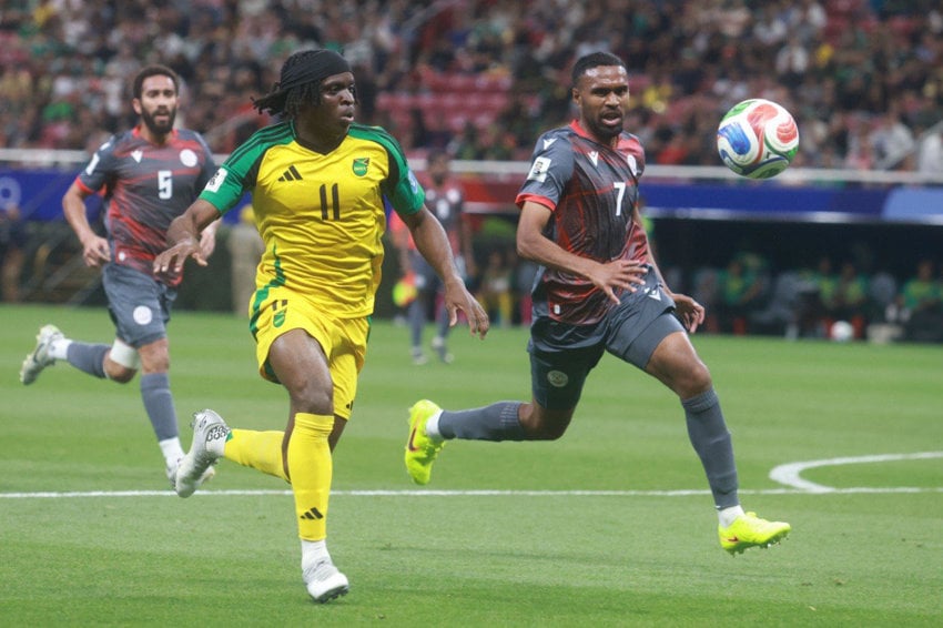 Jamaica national football team forward in a yellow jersey sprinting past defenders during a soccer match in a crowded stadium on March 26 in Guadalajara, a qualifying match for the 2026 World Cup men's competition.