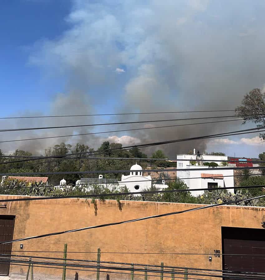 Black and white smoke rises into the sky above the roofs of white Mexican adobe homes in San Miguel de Allende, Mexico.