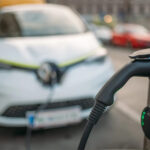 An EV charger in focus with an electric car in the background