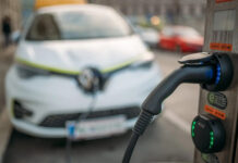 An EV charger in focus with an electric car in the background