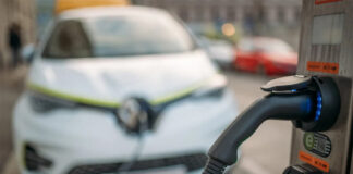 An EV charger in focus with an electric car in the background